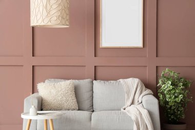 Oturma odasının iç tarafındaki kahverengi duvarın yanında rahat bir kanepe, masa ve çiçek var.