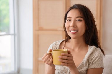 Evde bir fincan kahveli genç Asyalı kadın.