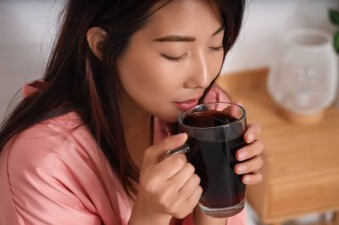 Genç Asyalı kadın yatak odasında kahve içiyor, yakın plan.