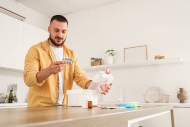 Genç adam mutfaktaki masada ilk yardım çantasından hap alıyor.