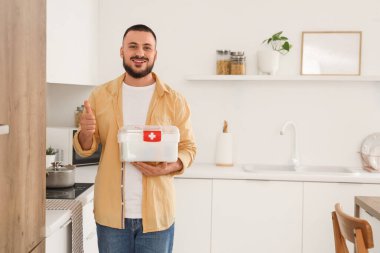 Mutfakta ilk yardım çantası olan genç bir adam baş parmağını kaldırıyor.