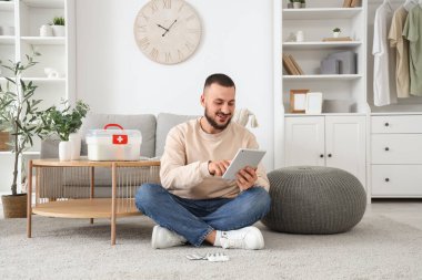 Evde tablet bilgisayar kullanan ilk yardım çantası olan genç bir adam.