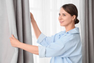 Gri perdeyi evde ayarlayan genç bir kadın.
