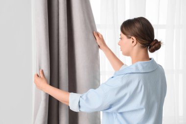 Gri perdeyi evde ayarlayan genç bir kadın.