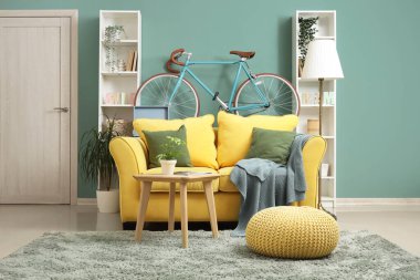 Bisikletli, sarı kanepeli ve raf üniteli şık bir oturma odası.