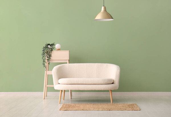 Белый диван и домашнее растение на столе у зеленой стены