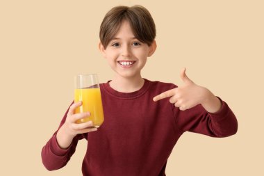 Bej arka planda portakal suyu bardağını gösteren küçük çocuk.