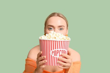 Yeşil arka planda patlamış mısır kovası olan mutlu genç bir kadın.