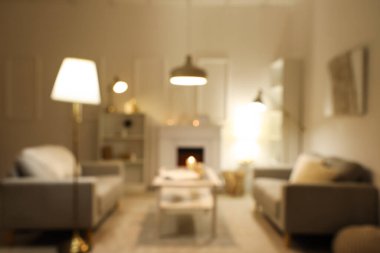 Gri kanepeleri, şöminesi, beyaz mobilyaları ve akşamları parlayan lambaları olan zarif oturma odasının bulanık görüntüsü.
