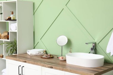 Raflar, lavabolu çekmeceler ve banyodaki yeşil duvarın yanında banyo malzemeleri.