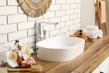 Banyodaki beyaz tuğla duvarın yanındaki çekmecelere lavabo ve banyo malzemeleri.