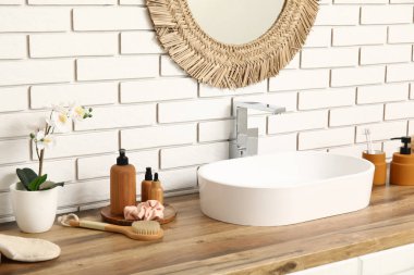 Banyodaki beyaz tuğla duvarın yanındaki çekmecelere lavabo ve banyo malzemeleri.