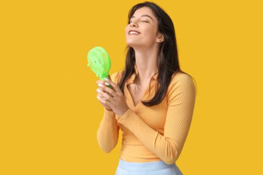 Sarı arka planda mini fanı olan genç bir kadın.