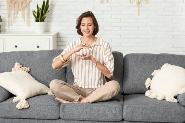 Evdeki kanepede oturmuş meditasyon yapan genç bir kadın.