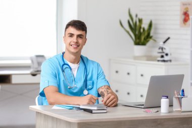 Klinikteki masada oturan genç erkek doktor.