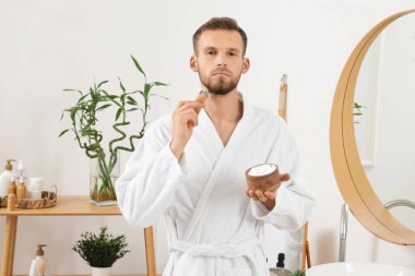 Banyo fırçasıyla tıraş köpüğü süren sakallı genç adam.