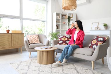 Gözlüklü genç kadın evdeki kanepede oturuyor.