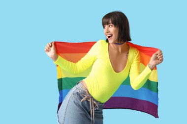 Mavi arka planda LGBT bayrağı olan gökkuşağı boyunduruklu güzel genç bir kadın.