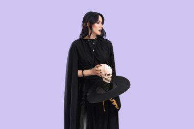 Cadılar Bayramı 'nda cadı gibi giyinmiş güzel bir kadın ve mor arka planda insan kafatası.