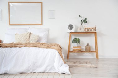 Elektrikli vantilatör ısıtıcısı ve okaliptüslü vazo yatak odasının içindeki masada.