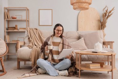 Oturma odasında sıcak ekose ve çay fincanı okuyan genç bir kadın.