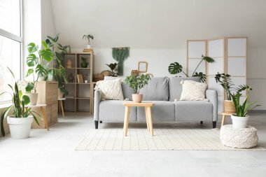 Yeşil çiçekli ve gri kanepeli, aydınlık oturma odasının içi.