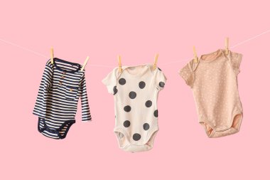 Pembe arka planda asılı duran bebek kıyafetleri.