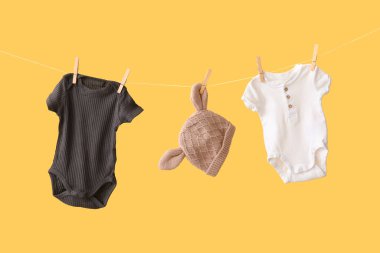 Sarı arka planda asılı duran şapkalı bebek kıyafetleri.