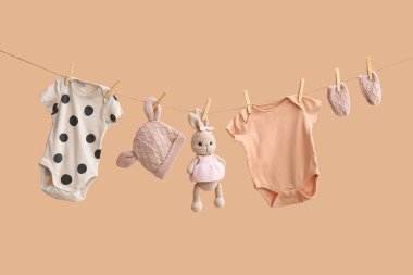 Aksesuarlı bebek kıyafetleri ve bej arka planda asılı duran bir oyuncak.