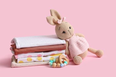 Oyuncak bebek kıyafetleri ve pembe arka planda çıngırak.