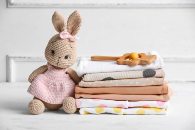 Bebek kıyafetleri yığını, çıngıraklı ve oyuncak ışıklı duvarın yanındaki masada.