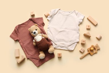 Bej arka planda oyuncakları olan bebek kıyafetleri.