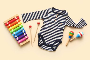 Bej arka planda ksilofon ve marakas olan bebek kıyafeti.