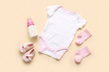 Aksesuarlı bebek kıyafeti ve bej arka planda bir şişe süt.