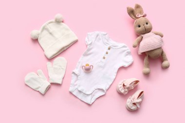 Aksesuarlı bebek kıyafeti ve pembe arka planda bir oyuncak.