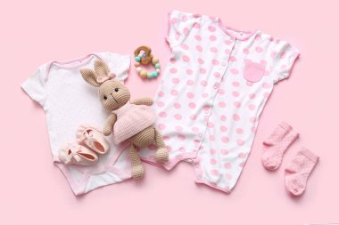 Aksesuarlı bebek kıyafetleri ve pembe arka planda oyuncak tavşan.