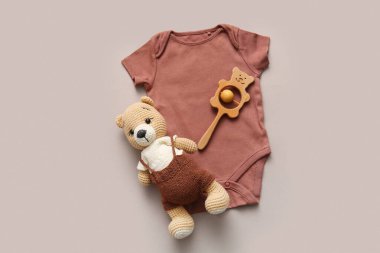 Bej arka planda çıngıraklı ve oyuncak ayılı bebek kıyafeti