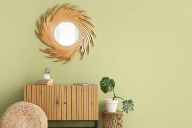 Çekmeceler, puf, saksı ve ayna yeşil duvarda.