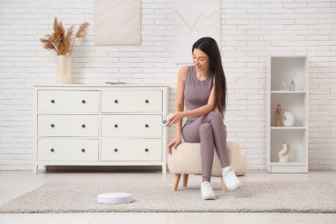 Sportif genç kadın evde robot elektrik süpürgesini açıyor.