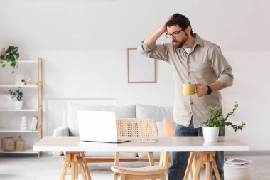 Evdeki masada fincan ve dizüstü bilgisayarlı genç adam kovuldu.