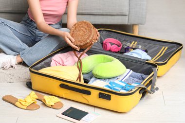 Çantalı genç bir kadın oturma odasında bavulunu topluyor.