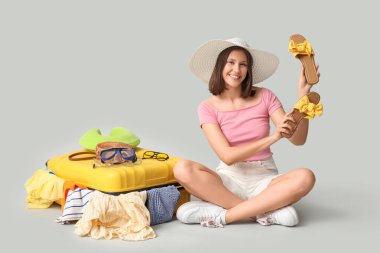 Ayakkabılı mutlu genç kadın beyaz arka planda seyahat için bavul hazırlıyor.