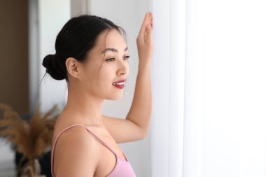 Evdeki ışık perdelerinin yanındaki genç Asyalı kadın, yakın çekim