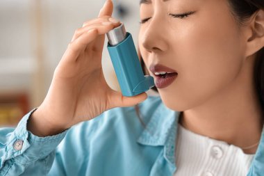 Genç Asyalı kadın evde astım spreyi kullanıyor, yakın plan.