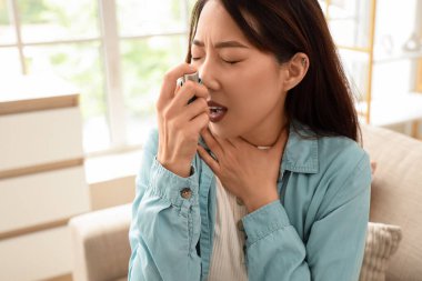 Astım krizi geçiren genç Asyalı kadın evde astım spreyi kullanıyor, yakın plan.