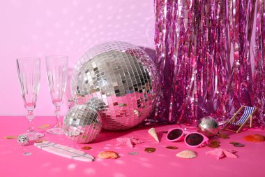 Şampanya bardaklı disko topları, plaj dekorları ve pembe arka planda süslemeler.