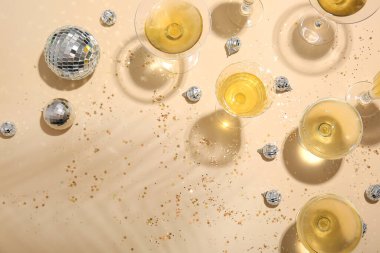 Şampanya bardaklı disko topları ve bej arka planda konfeti.