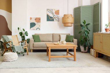 Pouf, yeşil katlı perde, oturma odasının iç tarafında kanepe ve masa.