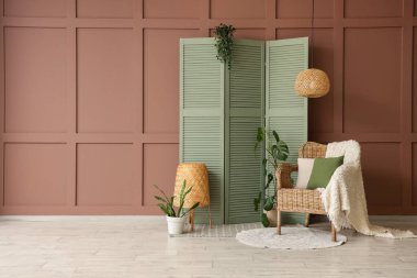 Katlanan ekran, koltuk, puf ve kahverengi duvarın yanındaki bitkiler.