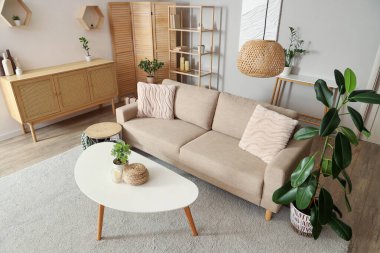 Bej kanepe, masa, çekmeceler ve oturma odasının iç tarafında katlanan ekran.